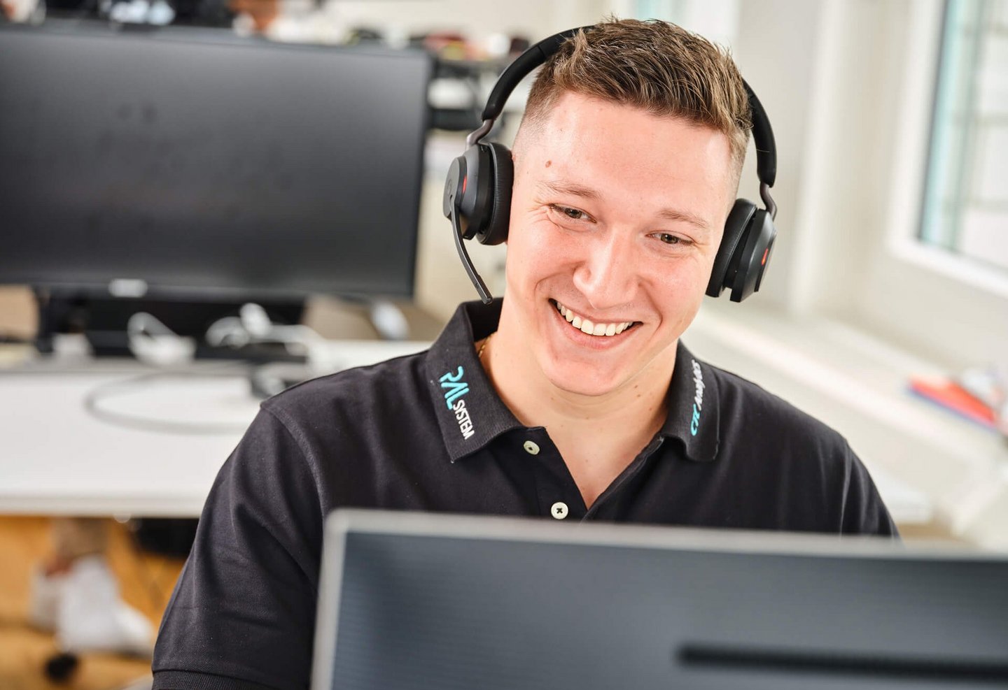 Smiling support staff member with a headset working at a computer, providing assistance for PAL Solutions