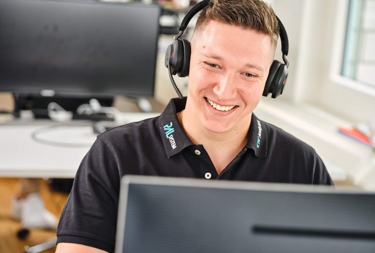 Smiling support staff member with a headset working at a computer, providing assistance for PAL Solution