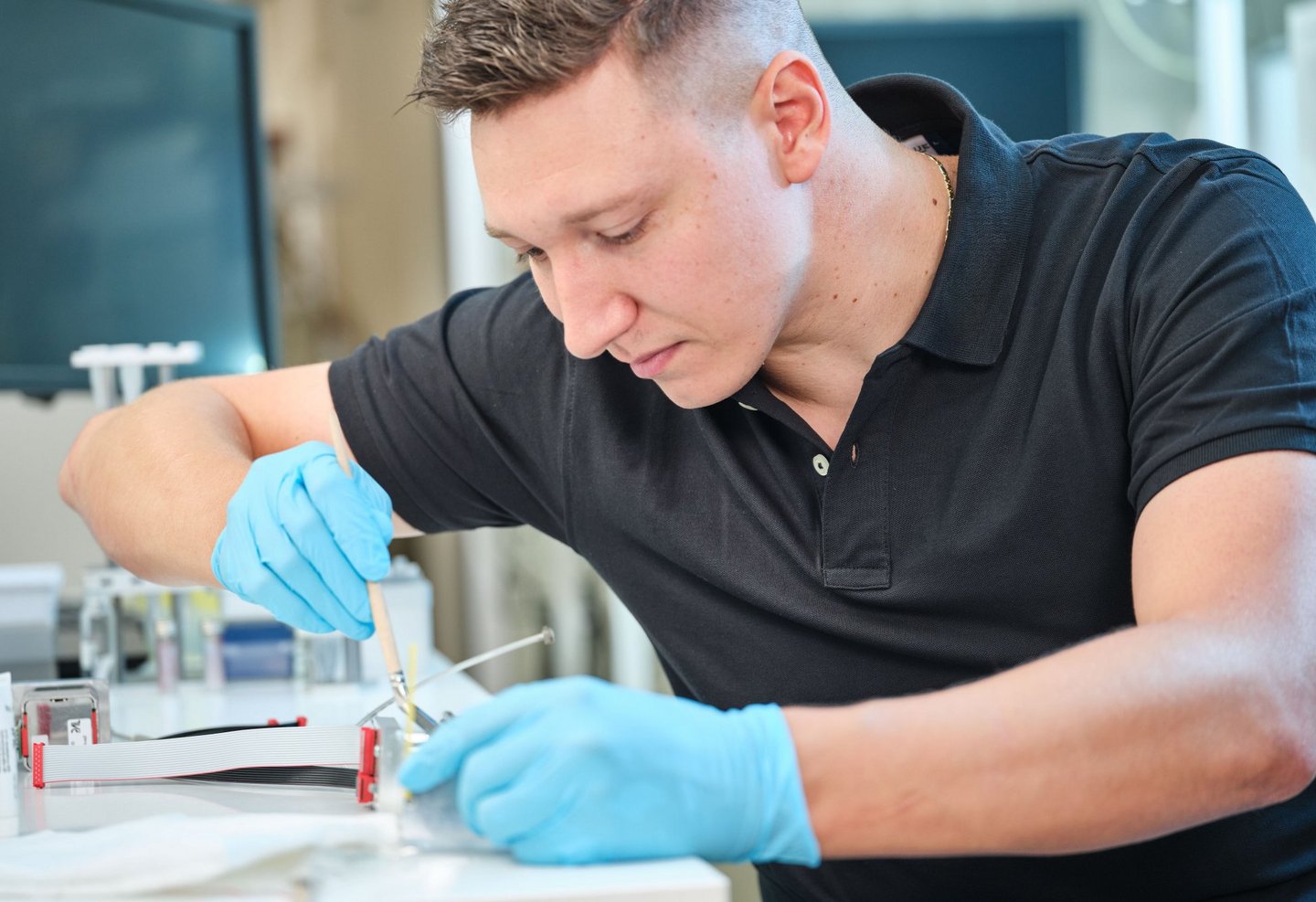 Technician wearing blue gloves assembling a small lab component, performing precise work for PAL Solutions .